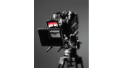 Professional video camera on a tripod against a dark gray background, with a red screen glowing on the camera monitor.